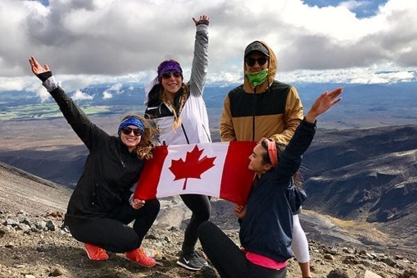 Youth holding a Canadian flag on a mountaintop in New Zealand